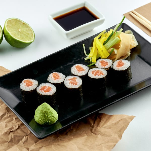 Min Sushi salmon maki rolls with wasabi, ginger, soy sauce, and lime on a black plate.