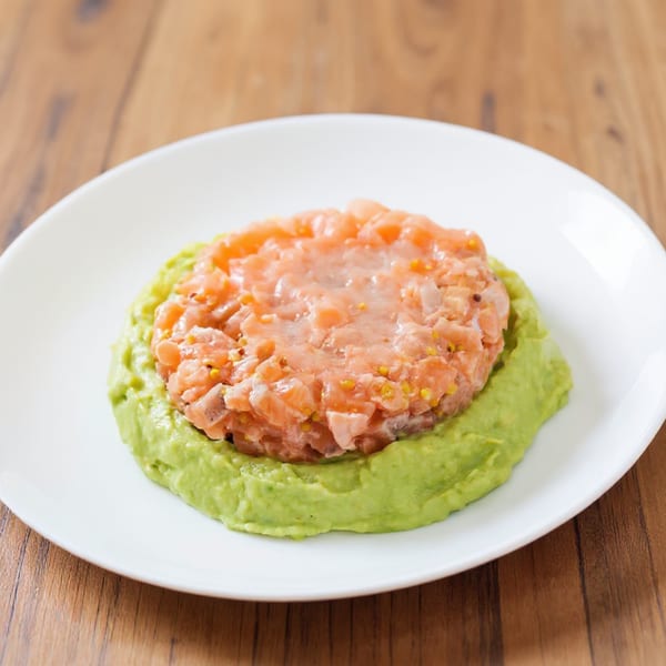Min Sushi's salmon tartare with avocado puree on a white plate, on a wooden table.