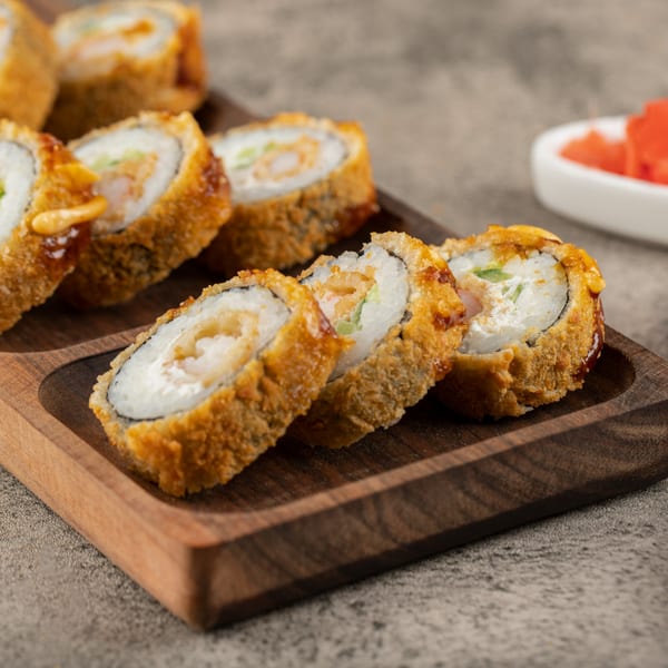 Min Sushi's crispy fried sushi rolls with creamy filling and sauce, served on a wooden tray with pickled ginger.