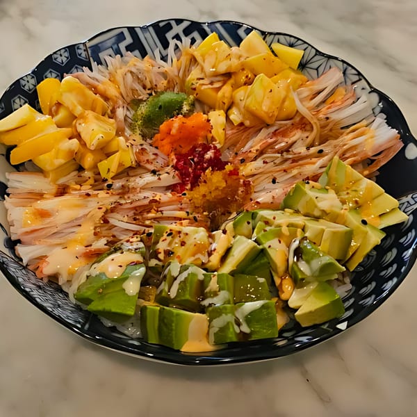 A colorful sushi bowl with avocado, mango, crab sticks, and roe in a decorative black and white bowl.